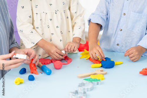 Fotografie Asian single mom teaches sharing teamwork using playdough tools, toddlers roll cut bright shapes, child development cognitive skill practice, parent child interaction early education, indoor playroom