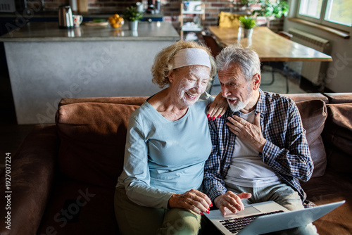 Senior couple using laptop at home, woman with facial mask