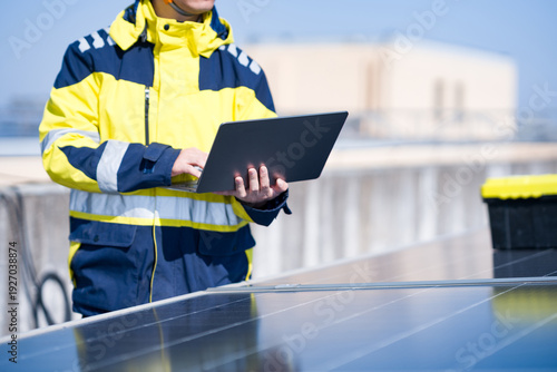 Obraz na plátne Worker in reflective uniform holding laptop inspecting solar panels on rooftop