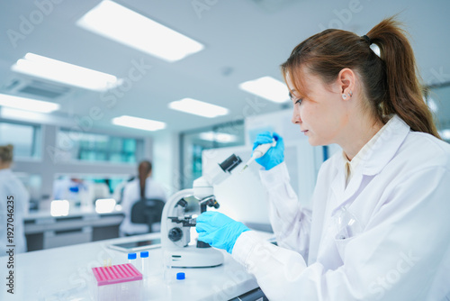 Pharmaceutical researcher performing precise chemical aliquot application on test slide. Young scientist validating biochemical compound reaction in modern biotech lab.