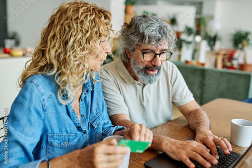 Tableau sur toile portrait of happy smiling senior elderly couple using a laptop computer and a cr