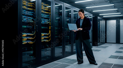 IT engineer inspecting server racks while working on laptop in enterprise data center