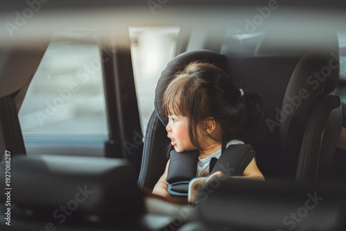 Canvastavla Happy little Asian girl sitting safely in car seat and looking out the window, toddler secured in child safety seat for road trip, concept of family travel, passenger safety