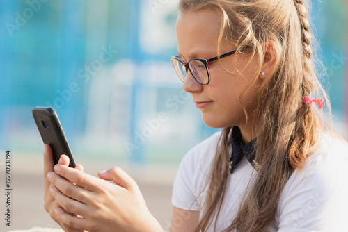 Cheerful portrait of a teenage schoolgirl with a phone and textbooks wearing reading glasses