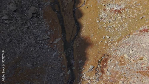 Top-down drone view following mountain stream near Col du Glandon in the Belledonne range, French Alps. Aerial alpine landscape with rocky terrain and autumn tones.