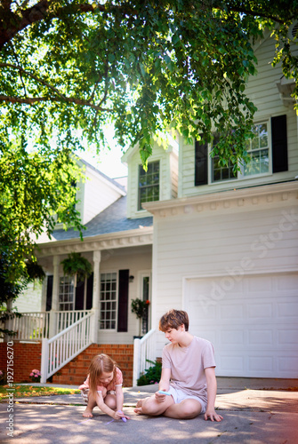 Brother and Little Sister Playing Tic Tac Toe Game with Chalk on Driveway under the Shadow of Big Tree in Summer- Happy Sibling Bonding and Outdoor Childhood Play at Home in Suburban Neighborhood