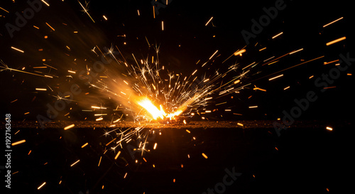Orange sparks bursting from metal grinding. Intense fire effects in dark environment. Industrial welding and fabrication process visualization for manufacturing and engineering concepts.