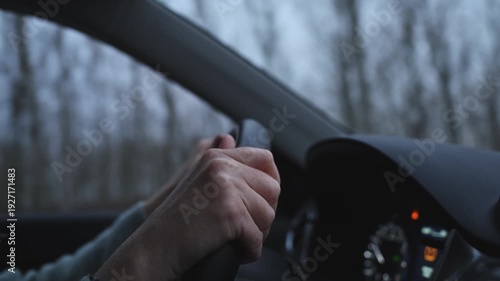 Woman firmly holding the wheel as she drives along a rural landscape in soft autumn evening light. 4K.