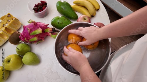 The hands of a woman in an apron standing in front of a table with fruit and washing mandarins