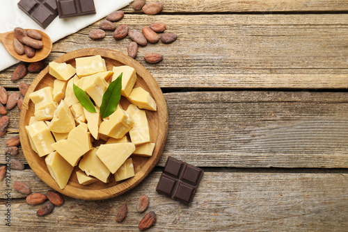 Organic cocoa butter, beans and chocolate pieces on wooden table, flat lay. Space for text