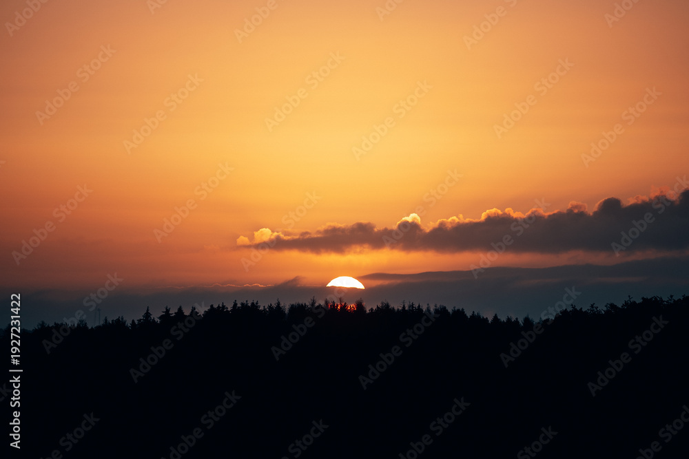 Fototapeta premium Breathtaking Sunrise Over a Dense Forest, Sky Ablaze with Vibrant Red and Orange Hues in Natural Light