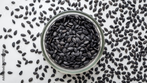 Black sunflower seeds in a glass bowl against a white backdrop. Aerial perspective of a nutritious snack or microgreens ingredient