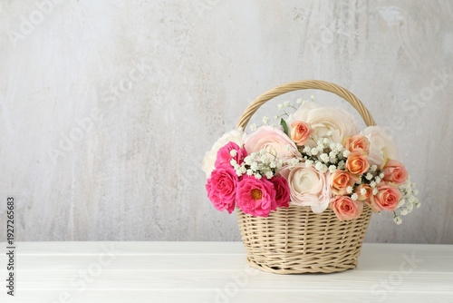Beautiful flowers in basket on white wooden table. Space for text