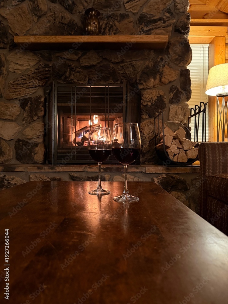 Fototapeta premium Glasses of red wine on wooden table near fireplace indoors