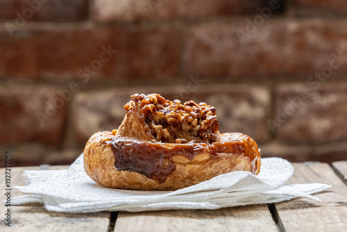 Pecan sticky bun with nuts.  Close-up, on napkin with brick wall in background