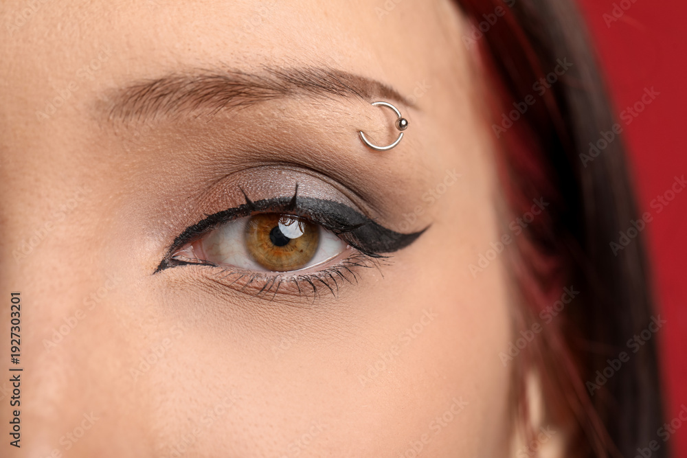 Obraz premium Woman with eyebrow piercing and perfect makeup on red background, closeup