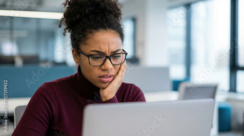 Stressed african american woman looking at laptop with worried expression in office