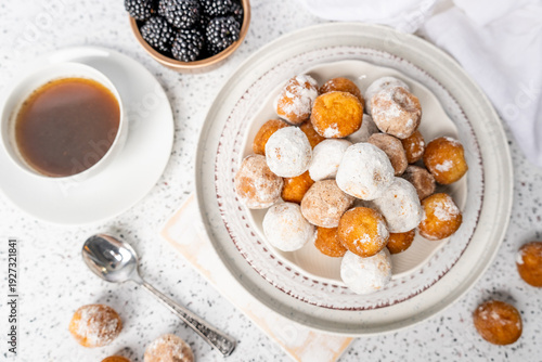 Plate of powdered sugar donut holes with coffee and blackberries