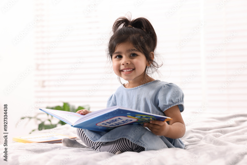 Naklejka premium Cute little girl reading book on bed at home
