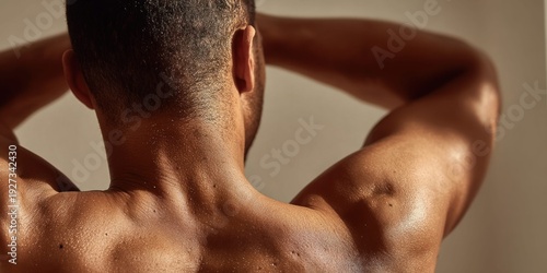 Close-up of a man's muscular back and shoulders with sweat glistening in warm sunlight