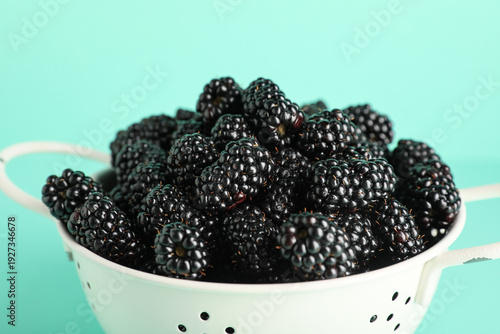 Photos Colander with sweet ripe blackberries on turquoise background, closeup