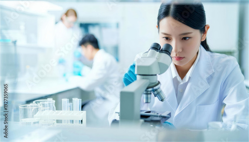 ガラス越しの研究室で顕微鏡を使って観察する女性研究者