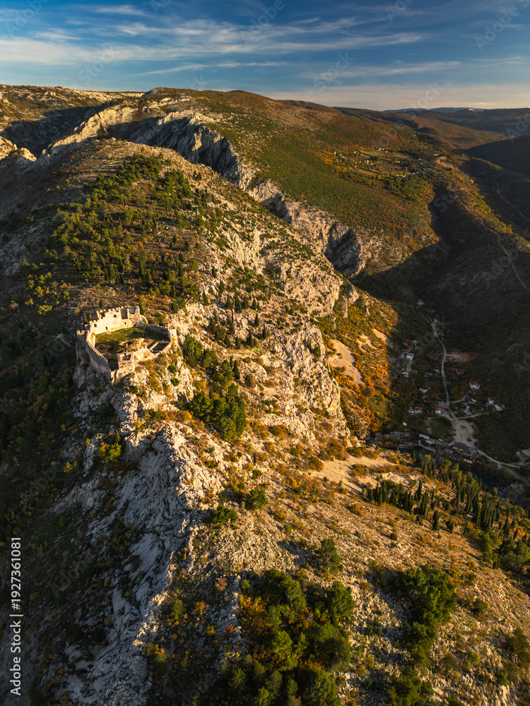 Obraz premium Vertical aerial view of the ancient medieval fortress on a mountain ridge. Epic historic ruins overlooking a deep canyon at sunset. Stjepan-grad, Blagaj, Bosnia.