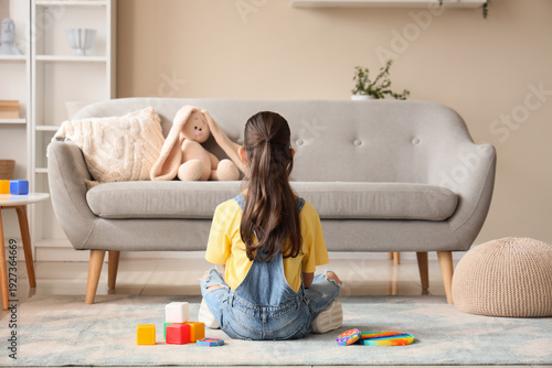 Cuadro en lienzo Cute girl with autistic disorder and toys sitting on floor at home, back view