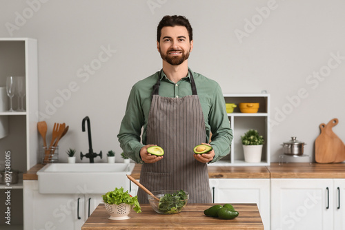Handsome man with fresh avocado, kale cabbage and lettuce at wooden table in ...