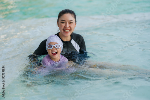 cheerful preschool child girl playing and swimming with her mother in pool