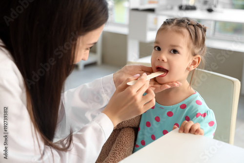 Female pediatrician checking little girl's throat in clinic