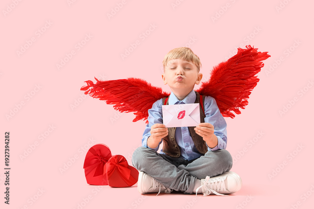 Obraz premium Cute little happy boy in cupid wings with gift boxes and love letter blowing kiss on pink background. Valentine's Day celebration