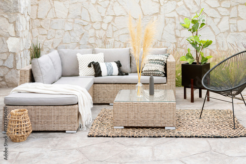 Spring Patio Furniture Set with Rattan Sectional Sofa, Decorative Pillow Covers, Wicker Patio Chairs, and Rattan Coffee Table, on a Botanical Area Rug in an Outdoor Living Space, Decorative Stone Wall