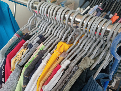 Φωτογραφία Close up of assorted clothing on grey plastic hangers hanging from a metal rack, colorful garments in a thrift store or retail shop setting