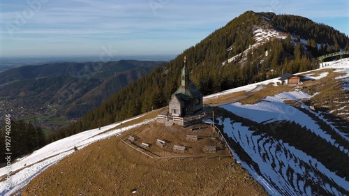 Kapelle Heilig Kreuz Rottach-Egern Tegernsee. Wallbergkapelle on mountain Wallberg overlooking lake Tegernsee and mountain range in sunny spring weather with snow at sunset. Chapel on peak of Alps. 