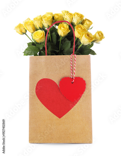 Yellow roses in paper bag with red heart on white background. Romantic gift