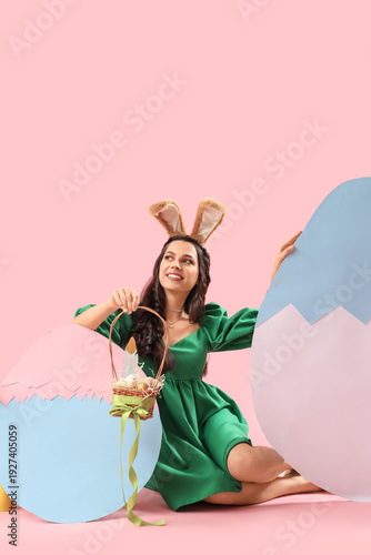 Beautiful woman in bunny ears with Easter eggs sitting on pink background