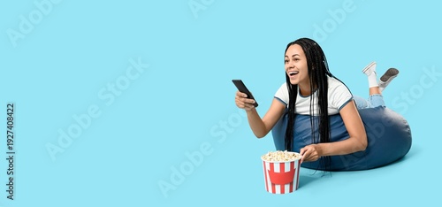 Happy African-American woman with bucket of popcorn watching movie on light b...
