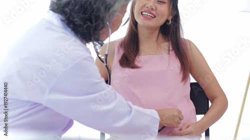 Elderly female doctor uses stethoscope to check pregnancy health of Asian woman. Health concept. Medical services.
