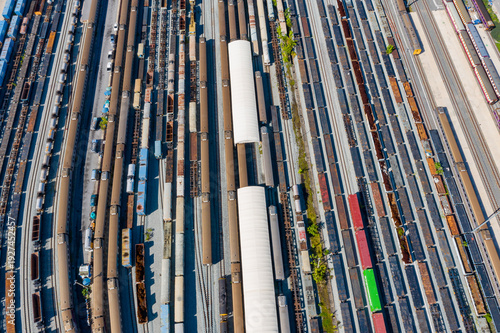 Schilderij op canvas Top down drone perspective of industrial train station with long freight cars aligned across wide rail yard, highlighting transportation system, urban planning, and logistics operations in daylight