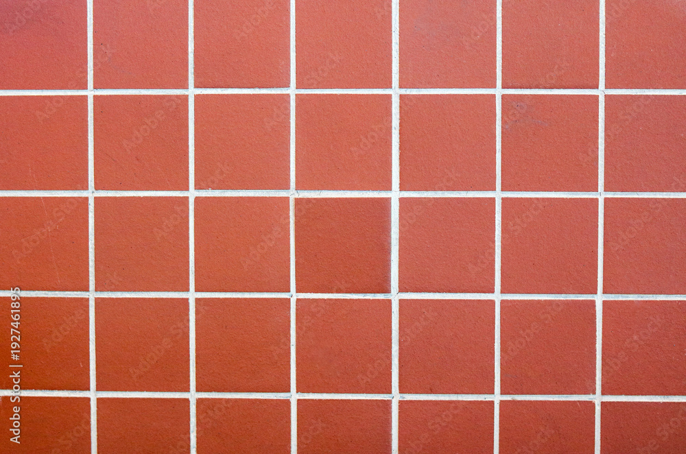 Fototapeta premium A neat arrangement of square terracotta tiles. The warm, reddish-brown clay features a fine, sandy texture and a matte finish.