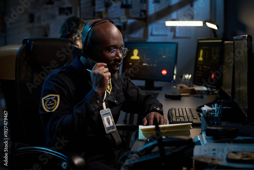 Obraz na plátne Young Black man wearing headset sitting at desk talking on phone while monitorin
