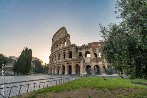 Colosseum at sunrise in Rome, Italy with memorial plaque inscription in latin which transtlates to "over the conservation of the Colosseum by popes Clement X, Benedict XIV, and Pius IX"