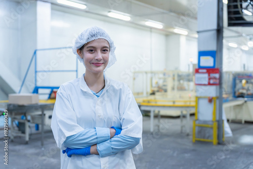 Portrait of a confident female food factory worker standing in a clean production plant, Smiling female quality control technician in white lab coat and protective hair net at work