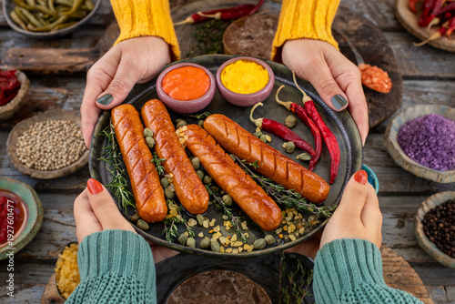 Grilled bratwurst and sausages in the plate at the hands of two women.  
