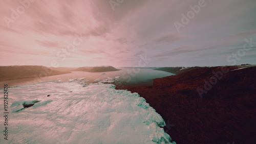 Pink sunset over icy shoreline, drone footage capturing bay and frozen edges with moody clouds and warm glow contrast of cold snow and soft light suggests