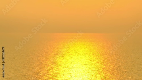 Drone shot of a glowing sunset spreading light over the ocean surface, showcasing natural beauty, gentle waves, soothing ambience, and themes of clarity, freedom, calmness, energy, connection, rhythm.