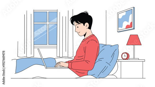 Relaxed young man working on his laptop while sitting in a comfortable bed with a blue pillow and a red desk lamp on the nightstand nearby.