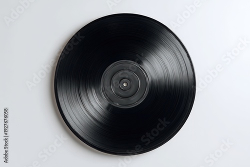 A glossy black analog audio disc rests on a white surface, showing concentric grooves