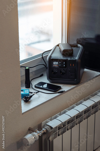 Wallpaper Mural Electricity backup at home in blackout, power outages, heating shutdown, energy crisis. Portable power station, power bank, small solar panel on window sill near home radiator. Vertical photo. Torontodigital.ca